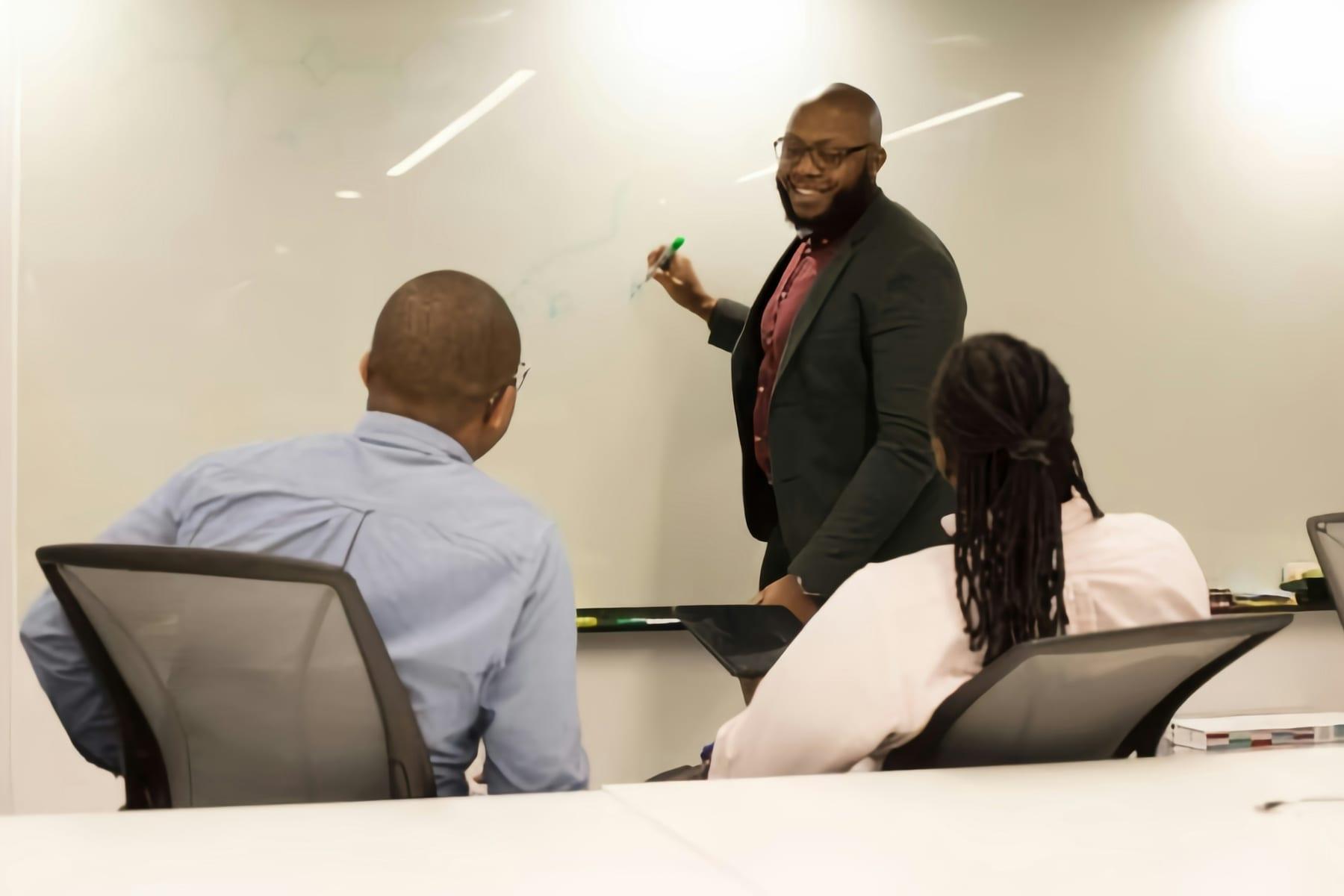 A manager standing at a whiteboard briefing two seated colleagues during a training session.